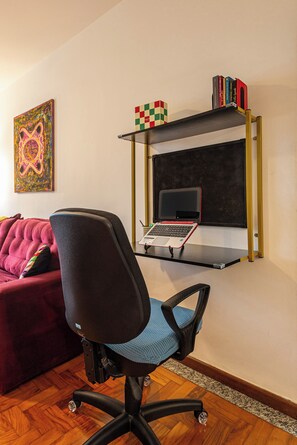 Una habitación con escritorio, una silla, una estantería y un cuadro colorido en la pared.