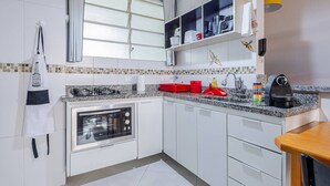 A modern kitchen with white cabinets, a built-in oven, a granite countertop, and a window with blinds. - Stylish & Charming in Consolação/Higienópolis • Parking • 3rd Guest Free (Sao Paulo)