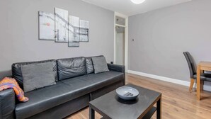 A modern living room with a black leather sofa, a coffee table, and a dining area with a wooden table and chairs. - Spacious & Central | 1 Bed | WiFi | Regent's Canal (London)