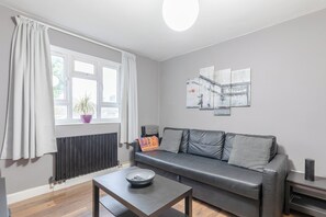 A modern living room with a grey sofa, a coffee table, and a radiator. - Spacious & Central | 1 Bed | WiFi | Regent's Canal (London)