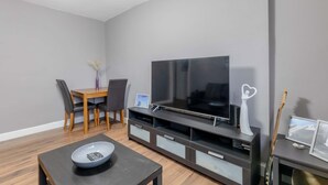 A modern living room with a flat-screen TV, wooden dining table, and chairs. - Spacious & Central | 1 Bed | WiFi | Regent's Canal (London)