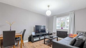 A modern living room with a flat-screen TV, wooden dining table, and a sofa. - Spacious & Central | 1 Bed | WiFi | Regent's Canal (London)