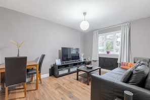 A modern living room with a flat-screen TV, wooden dining table, and a sofa.