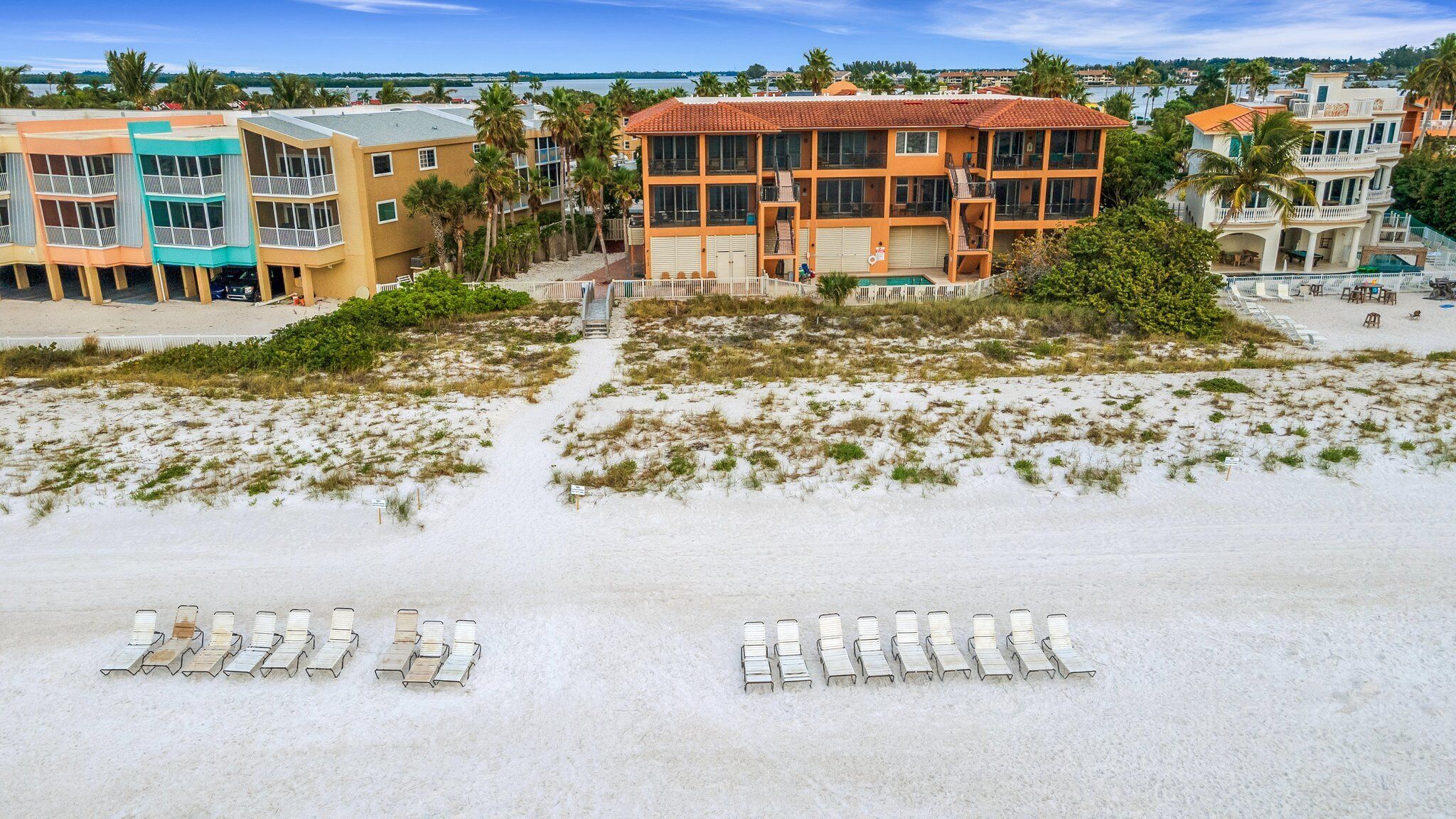 A beachfront hotel with multiple buildings, a pool, and beach chairs.