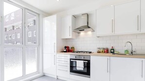 A modern kitchen with white cabinets, a stainless steel range hood, a built-in oven, and a window with frosted glass.