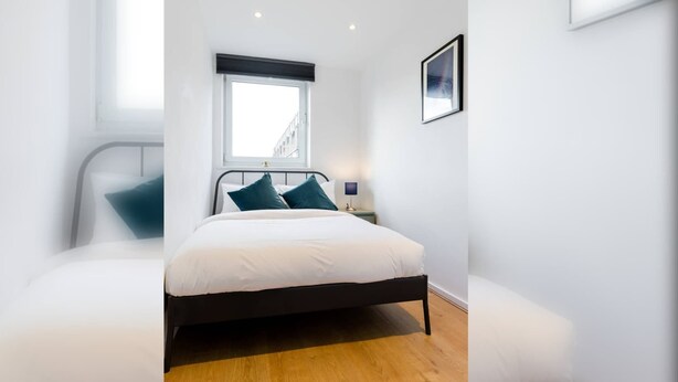 A bedroom with a bed, a window, a bedside table, and a wall-mounted picture.