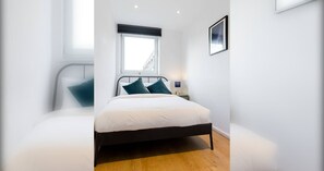A bedroom with a bed, a window, a bedside table, and a wall-mounted picture.