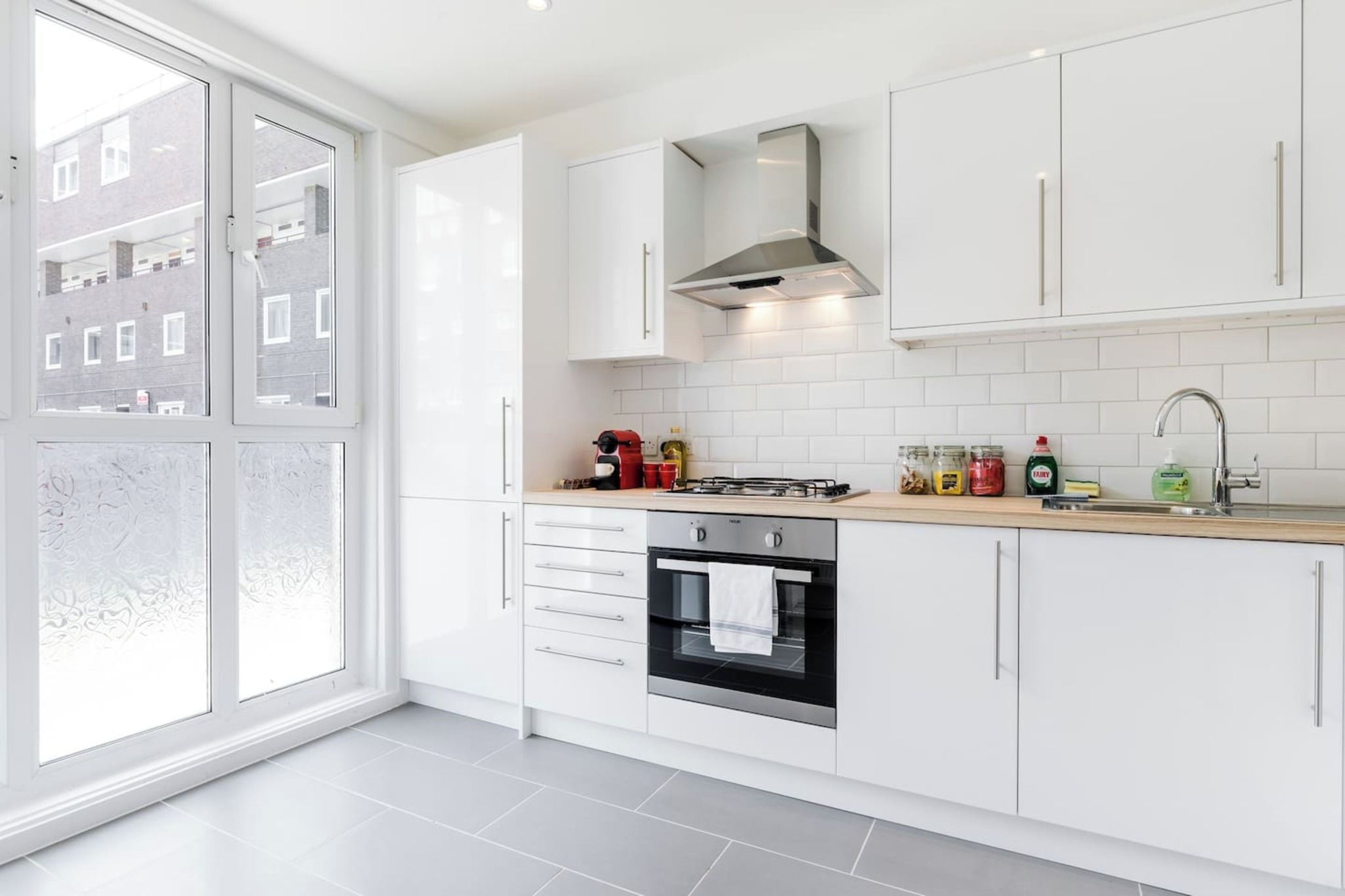 A modern kitchen with white cabinets, a stove, oven, and a large window.