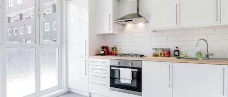 A modern kitchen with white cabinets, a stove, oven, and a large window.