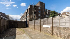 A courtyard with a brick wall, a concrete pathway, and a multi-story residential building in the background.