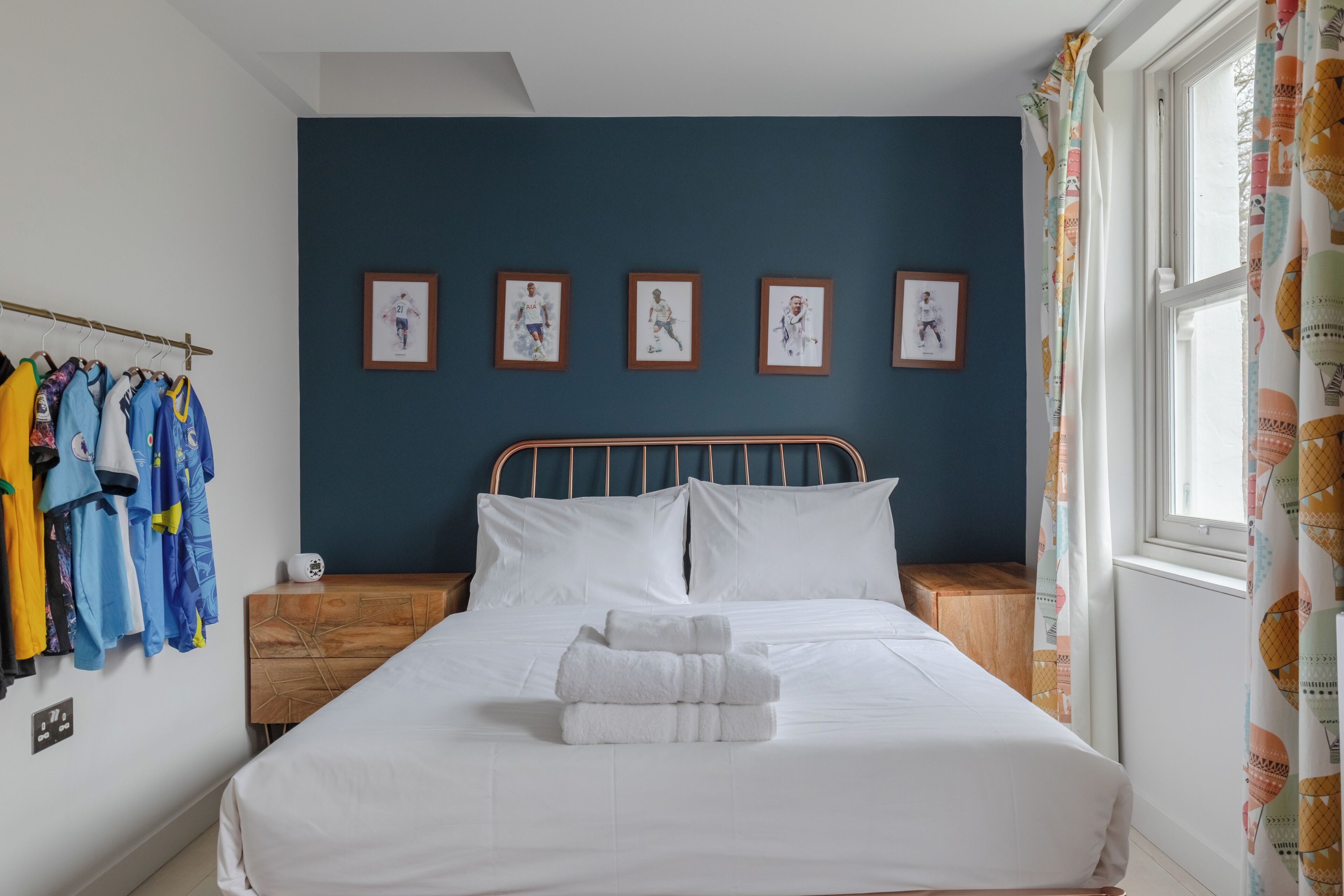 A neatly made bed with white linens and a folded towel, a wooden nightstand with a white lamp, and a wall with four framed pictures.
