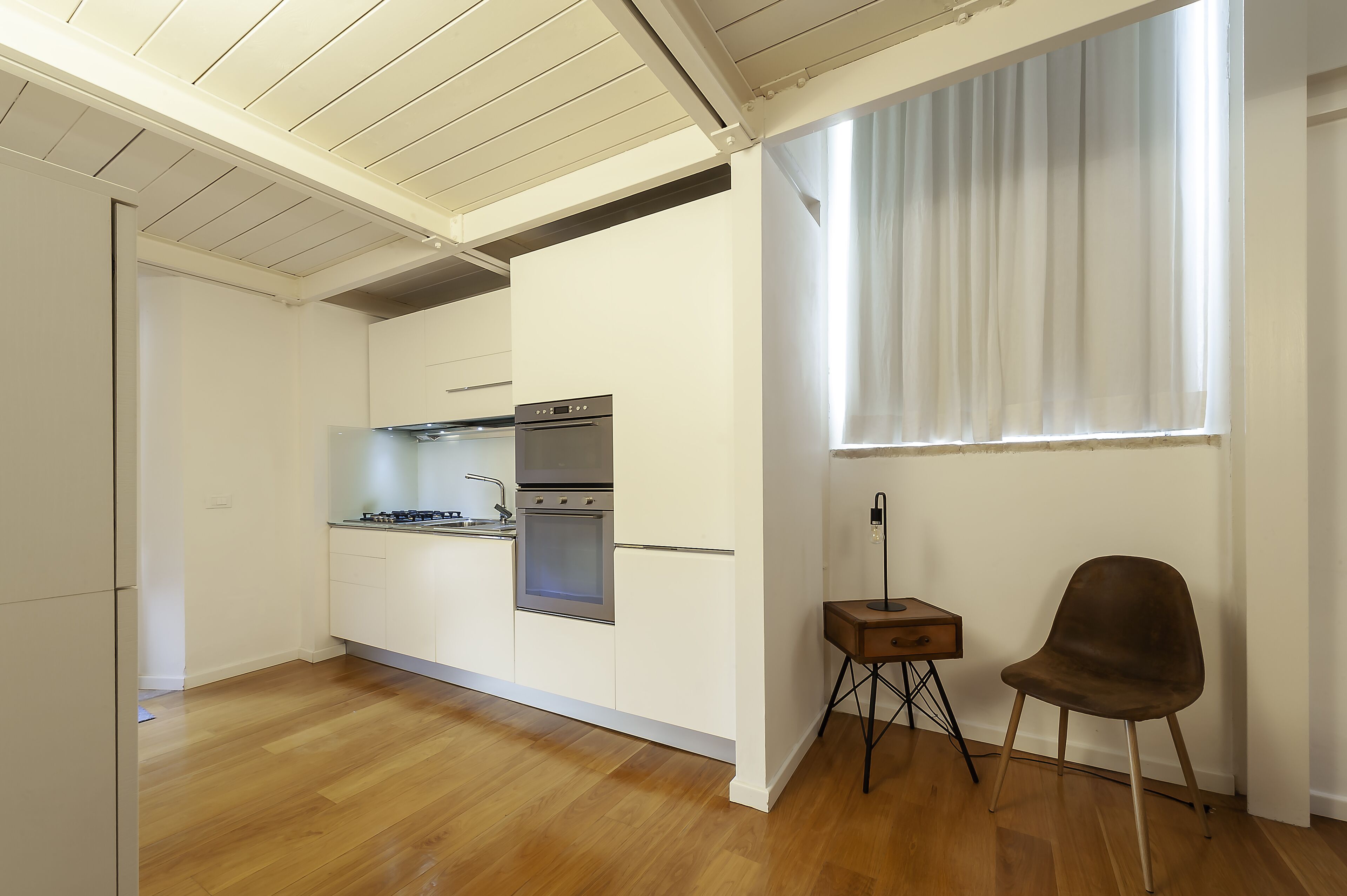 Una cocina moderna con armarios blancos, electrodomésticos de acero inoxidable y piso de madera.