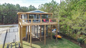 A wooden deck structure with a covered area and a lower level, surrounded by trees. - Bay St Louis Home w/ Private Dock + Kayaks! (Bay St Louis)