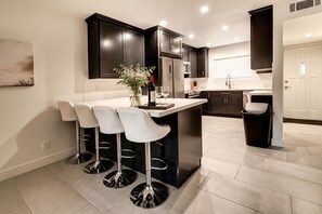 Una cocina moderna con armarios oscuros, una isla central con taburetes altos y un refrigerador de acero inoxidable.