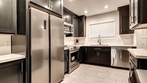 A modern kitchen with dark cabinetry, stainless steel appliances, and a window with blinds. - Luxury Old Town 2BR/2BA • AC • 2 Pools • Parking (Scottsdale)