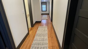 Un couloir au sol en bois, agrémenté de tapis à motifs, qui mène à une porte avec une fenêtre au bout.