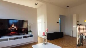 A living room with a flat-screen TV, a white coffee table, a black sofa, and a potted plant. - Spacious private apartment, 90m2, 25min from Amsterdam (Hilversum)