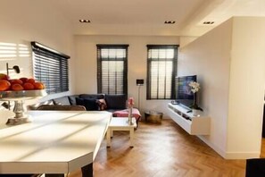 A modern living room with a sofa, a dining table, and a TV on a stand. - Spacious private apartment, 90m2, 25min from Amsterdam (Hilversum)