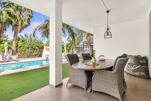 A patio with wicker furniture, a pool, and a view of palm trees.