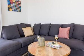 A modern living room with a dark grey sectional sofa, a round wooden coffee table, and a small metal pitcher.