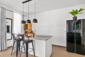 A modern kitchen with a granite countertop, black bar stools, pendant lighting, and a refrigerator with a plant on top. - Spacious Private Apartment with Pool 2-4p | #2 (Jan Thiel)