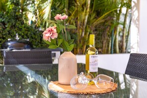 A glass table with a bottle of wine, a vase with flowers, and a pair of glasses.