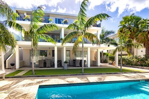 A modern two-story house with a swimming pool, outdoor furniture, and palm trees.