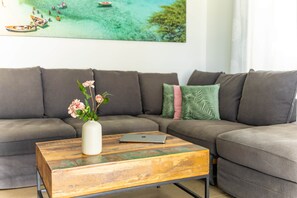 A living room with a gray sectional sofa, a wooden coffee table with a laptop, and a vase with flowers.