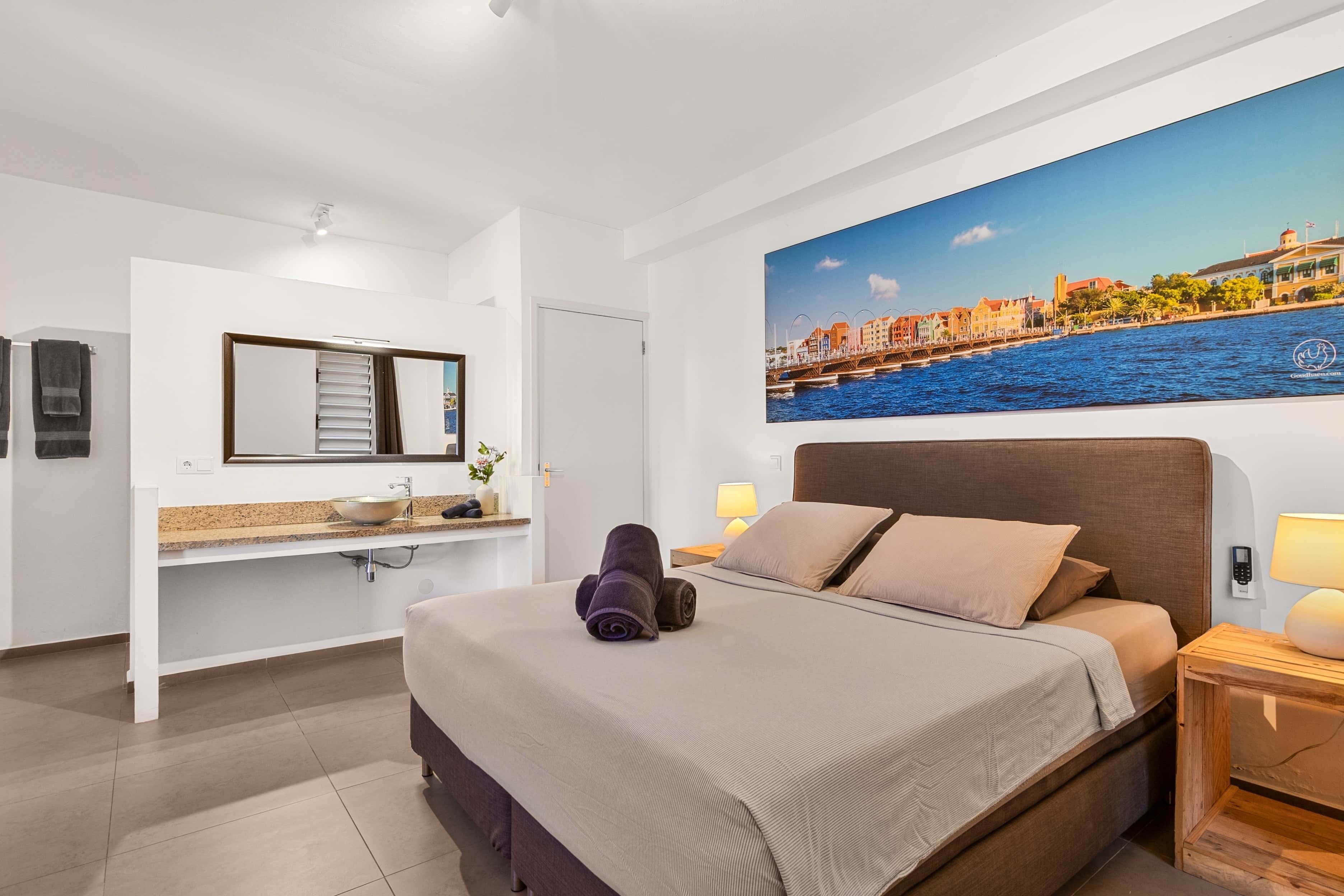 Een hotelkamer met een bed, een badkamer en een groot raam met uitzicht op de stad.