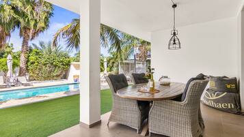 A patio with wicker furniture, a pool, and a view of palm trees.