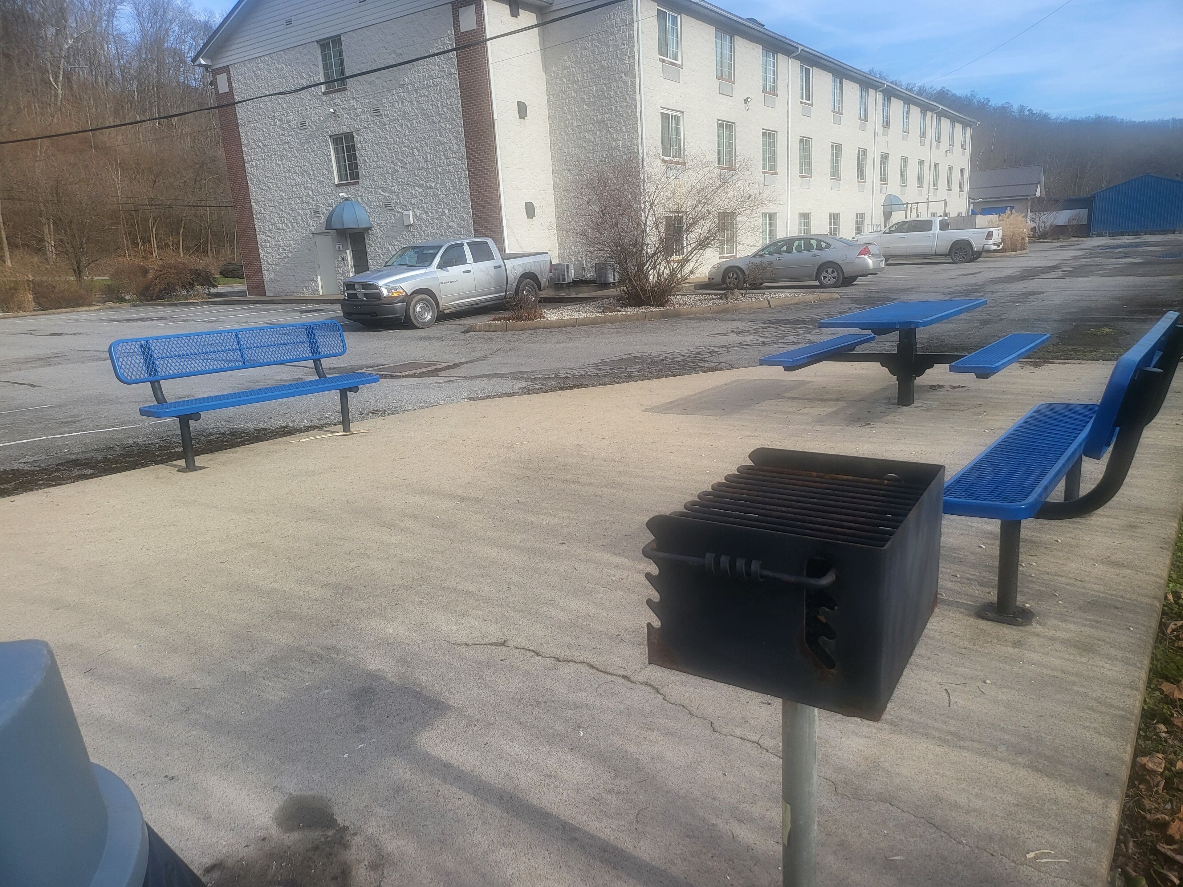 A parking lot with blue benches and picnic tables, a stone building, and a white pickup truck.
