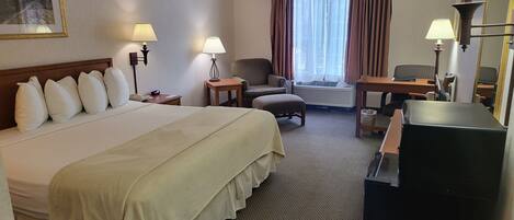 A hotel room with a large bed, a desk, a chair, a sofa, and a television.