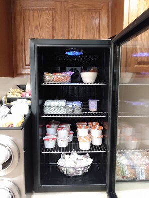 Un refrigerador lleno de diversos alimentos, como recipientes de yogur, productos envasados y un tazón.