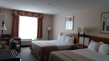 Quarto de hotel com duas camas, uma escrivaninha, uma cadeira, um abajur e uma janela com cortinas.