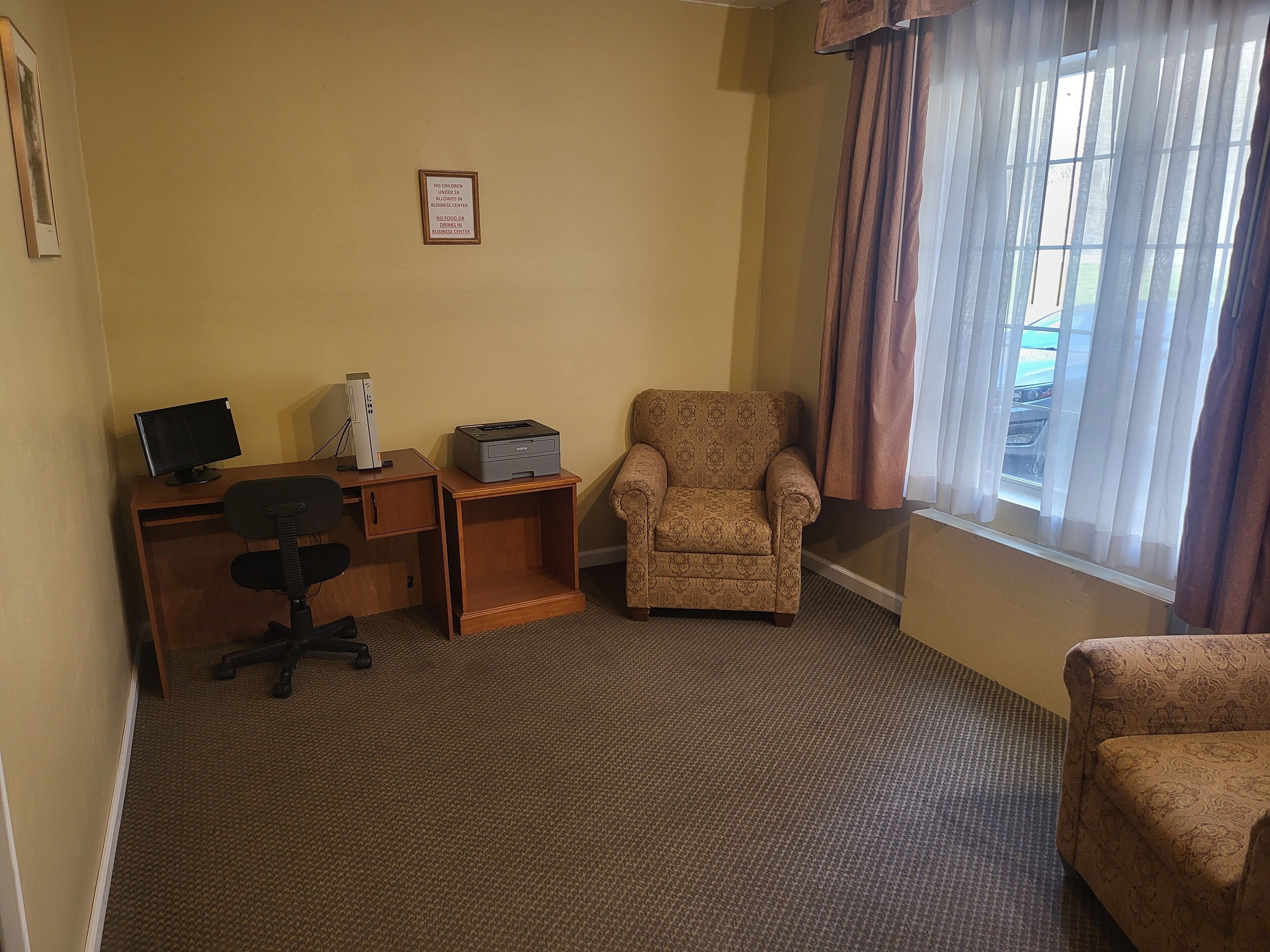 A small office with a desk, computer, printer, and two patterned armchairs.