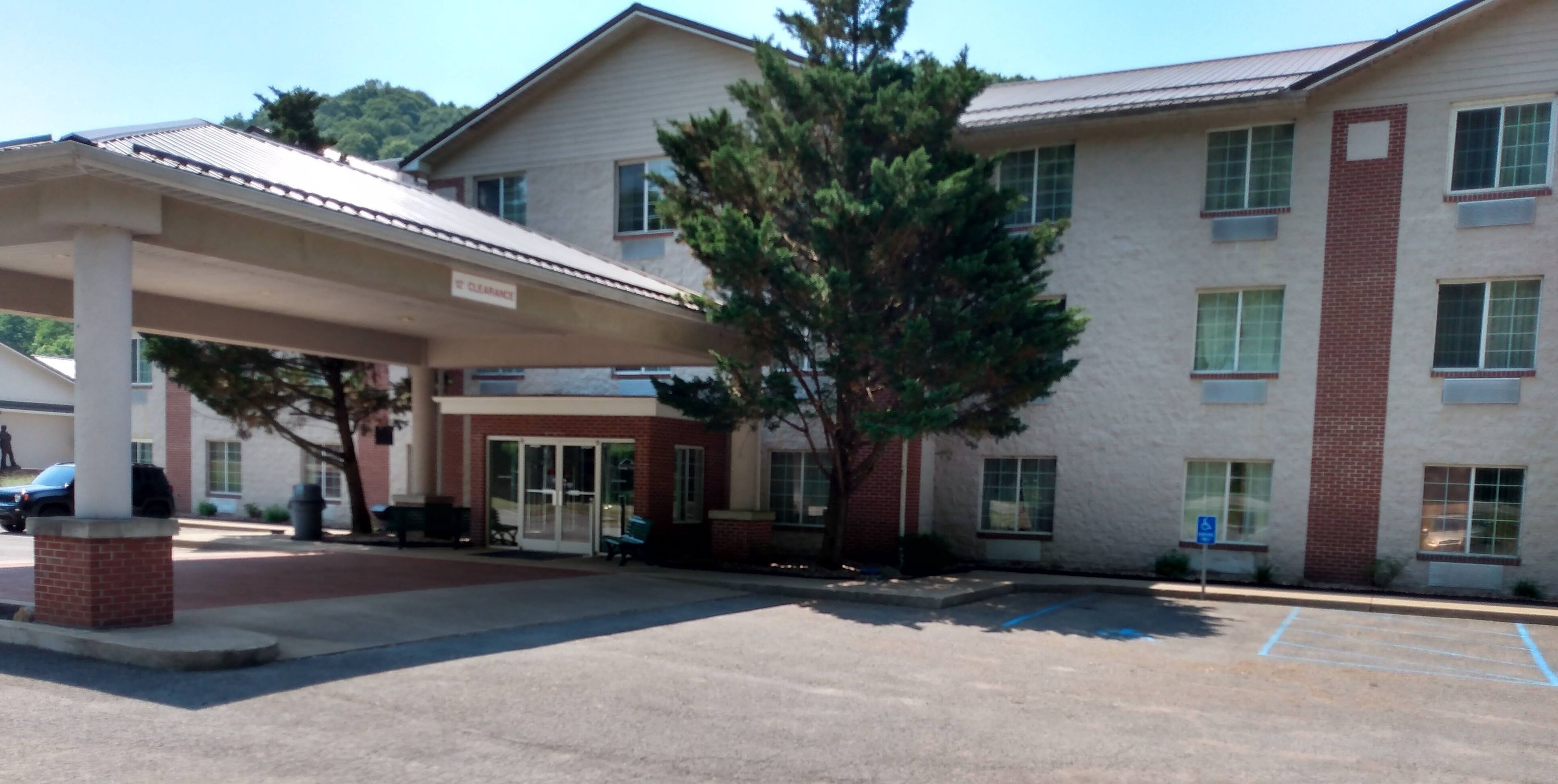 A building with a covered parking area, a clear sky, and a tree in front.