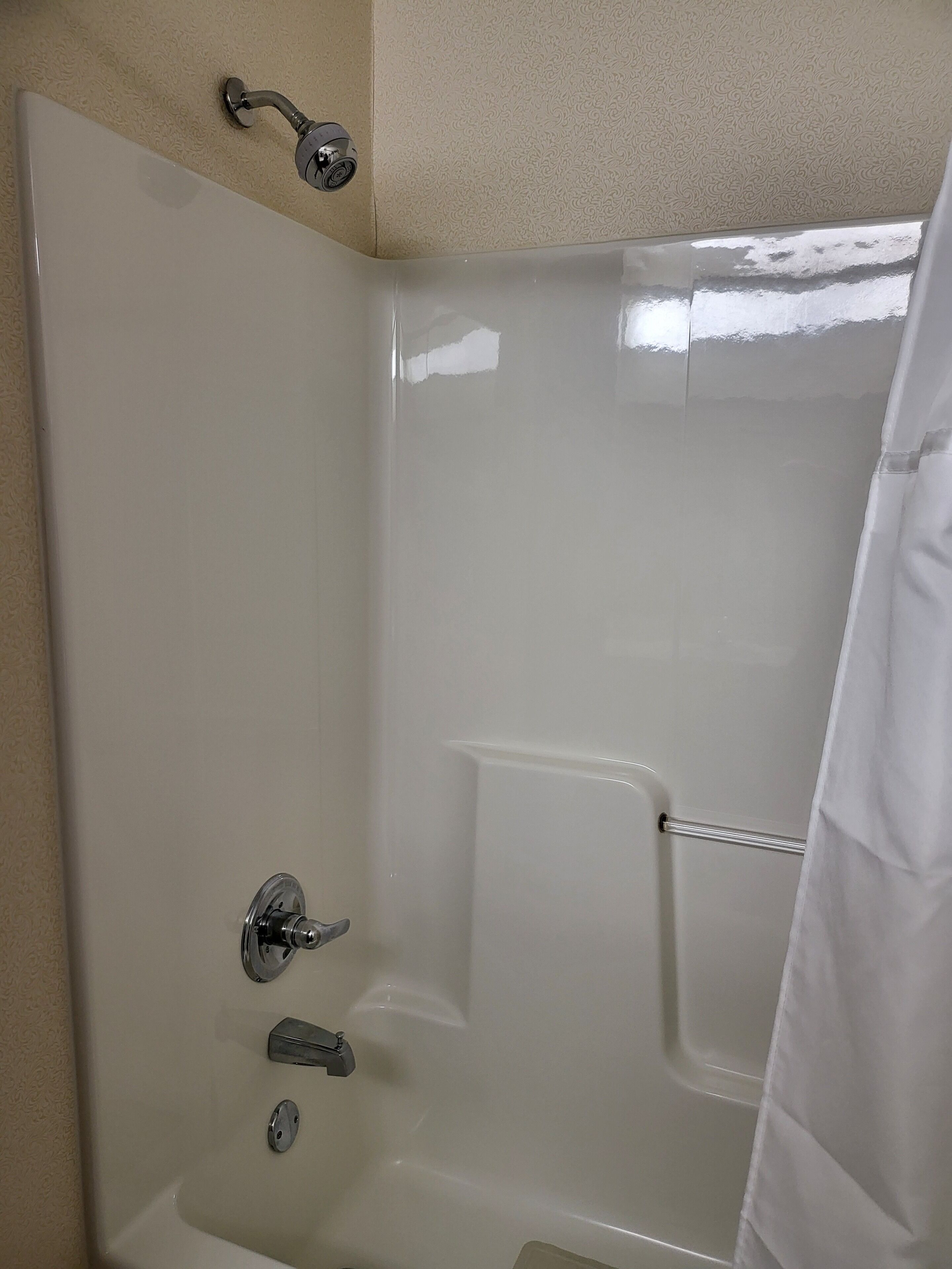 A corner shower with a chrome faucet, a handheld showerhead, and a white shower curtain.