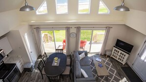 Ein großzügiger Wohnbereich mit Esstisch, Sofa und TV-Standfuß. Große Fenster bieten einen Blick ins Freie.