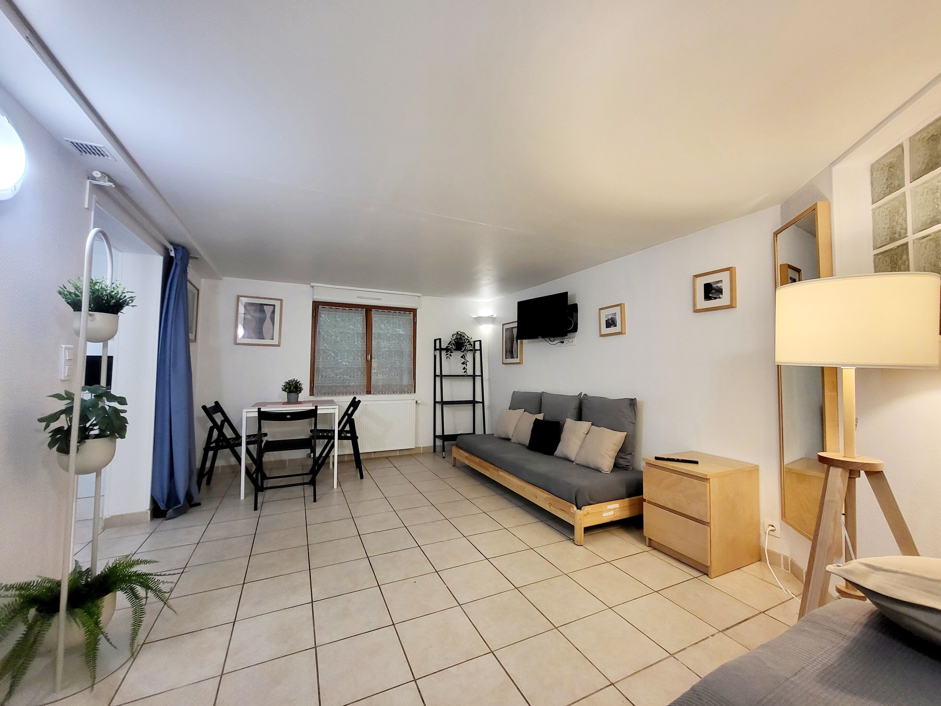 A compact living space with a sofa, a small table with chairs, a TV mounted on the wall, and a lamp.