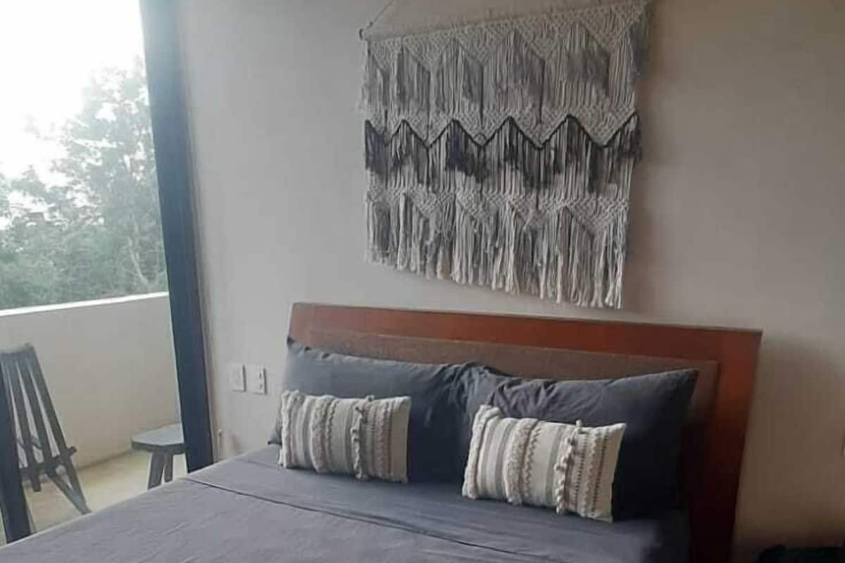 A bedroom with a large bed, a macrame wall hanging, and a view of the outdoors.