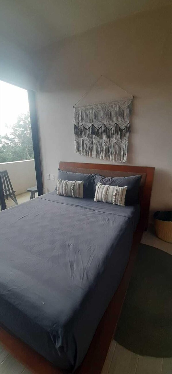 Une chambre avec un grand lit, une décoration murale en macramé et une vue sur l’extérieur.