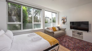 A modern hotel room with a large bed, a sofa, a TV, and large windows. - Lovely Studio with Free Parking in East Melbourne! (East Melbourne)