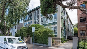 A white van parked in front of a building with a green and beige facade, a staircase, and a sign indicating parking availability. - Lovely Studio with Free Parking in East Melbourne! (East Melbourne)