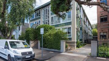 A white van parked in front of a building with a green and beige facade, a staircase, and a sign indicating parking availability.