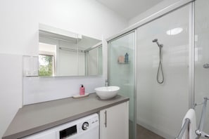 A modern bathroom with a white sink, a glass shower enclosure, and a built-in dishwasher.