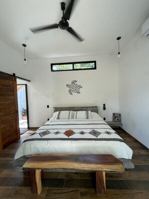 A bedroom with a bed, a ceiling fan, a window, and a wooden bench.