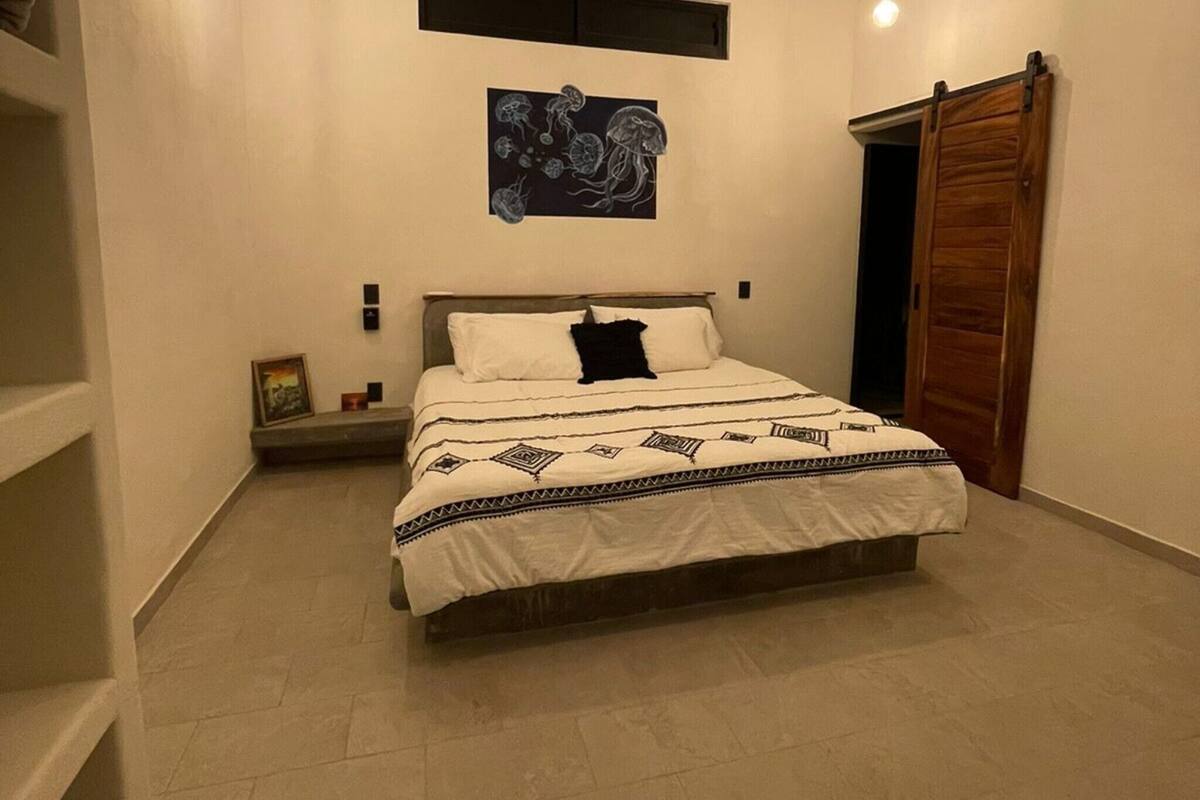 Un dormitorio con cama, ventilador de techo, lámpara de pared e imagen enmarco.