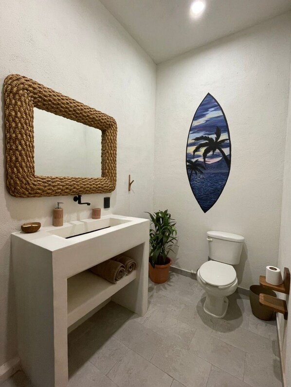 A bathroom with a white sink, a mirror, a toilet, and a potted plant.