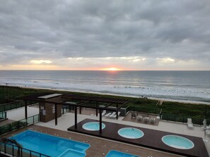 A rooftop pool area with a view of the ocean at sunset.