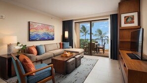 A modern hotel room with a sofa, armchair, coffee table, and a balcony with a view of palm trees.